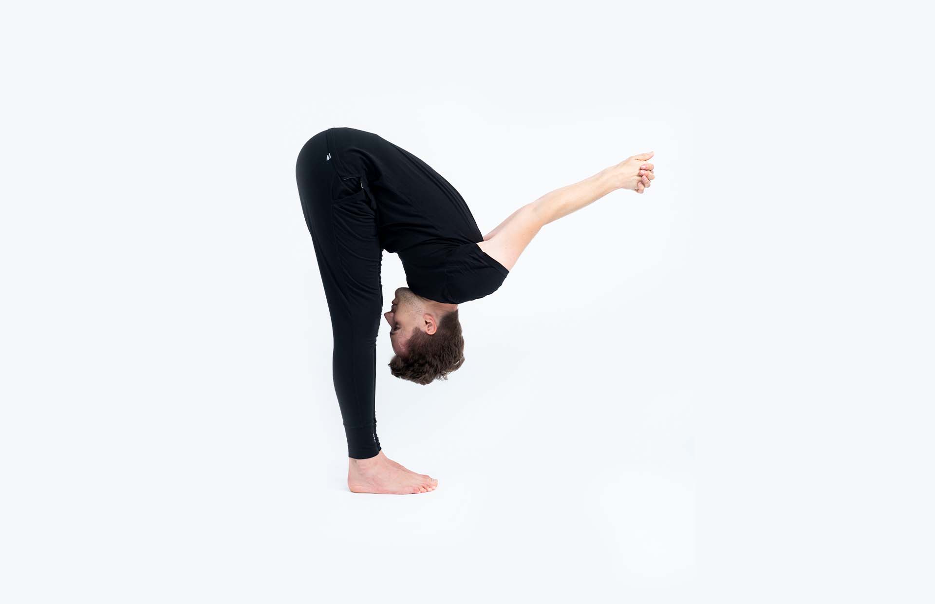 A person folding forward into Uttanasana with clasped hands behind their back