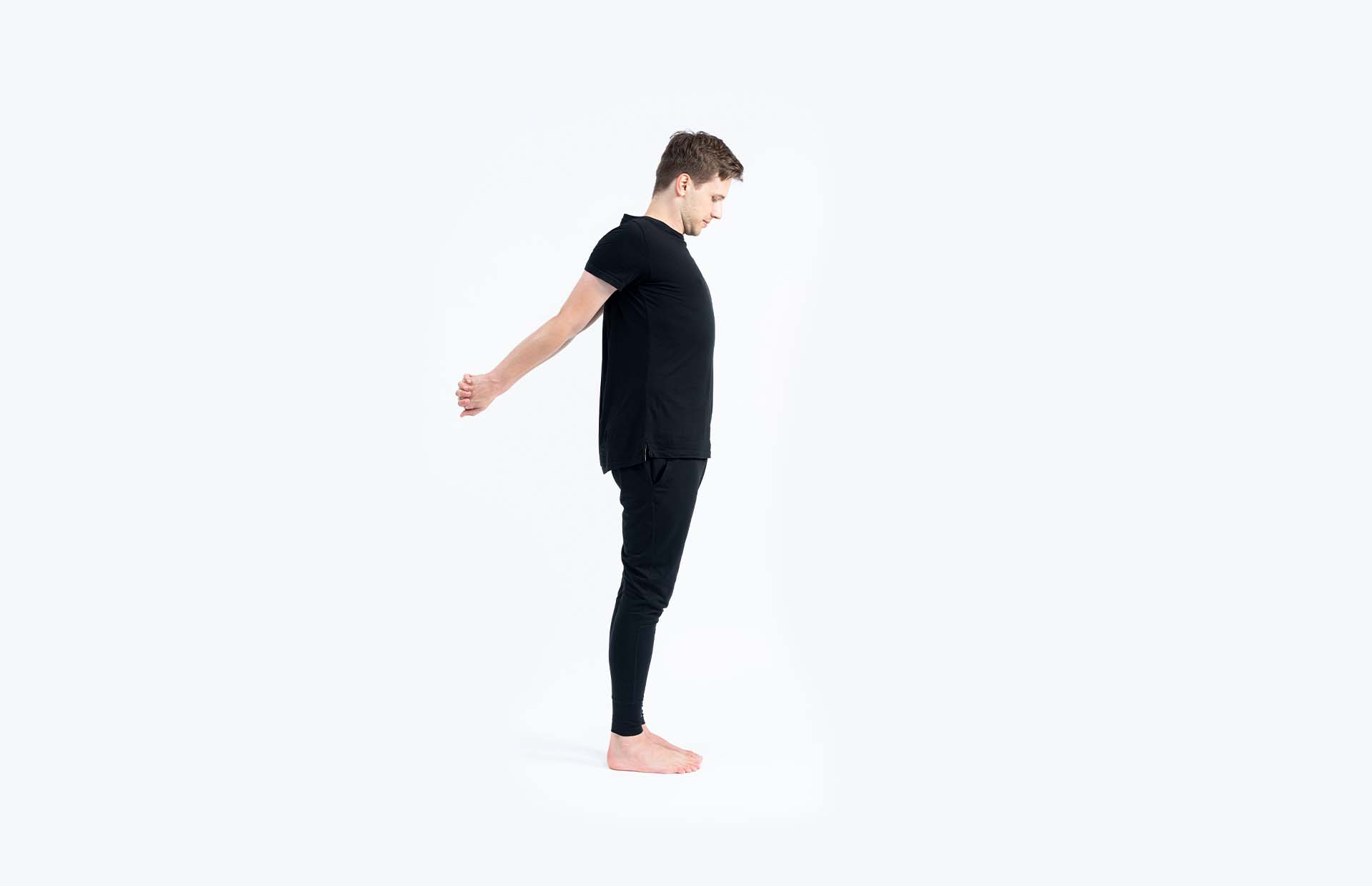A person standing with hands clasped behind back and extended away from body (Tadasana Variation)